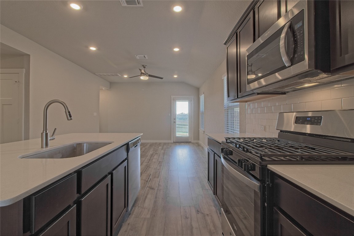 112 Halford Road Georgetown, TX 78633 - Photo 10 of 37 Kitchen featuring appliances with stainless steel finishes, light stone countertops, light wood-type flooring, vaulted ceiling, and dark brown cabinetry