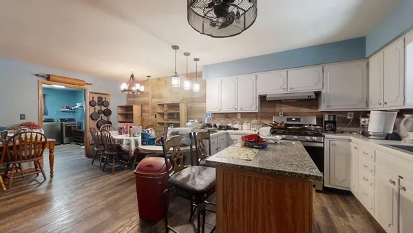a kitchen with stainless steel appliances granite countertop a stove top oven a sink a dining table and chairs with wooden floor