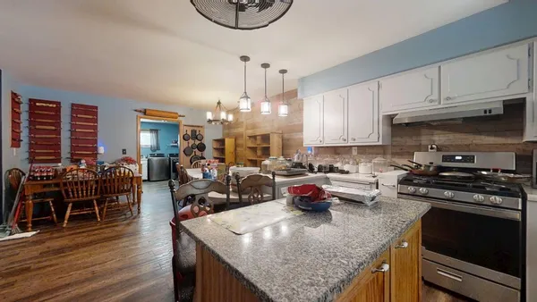 a kitchen with stainless steel appliances granite countertop a stove top oven a dining table and chairs with wooden floor