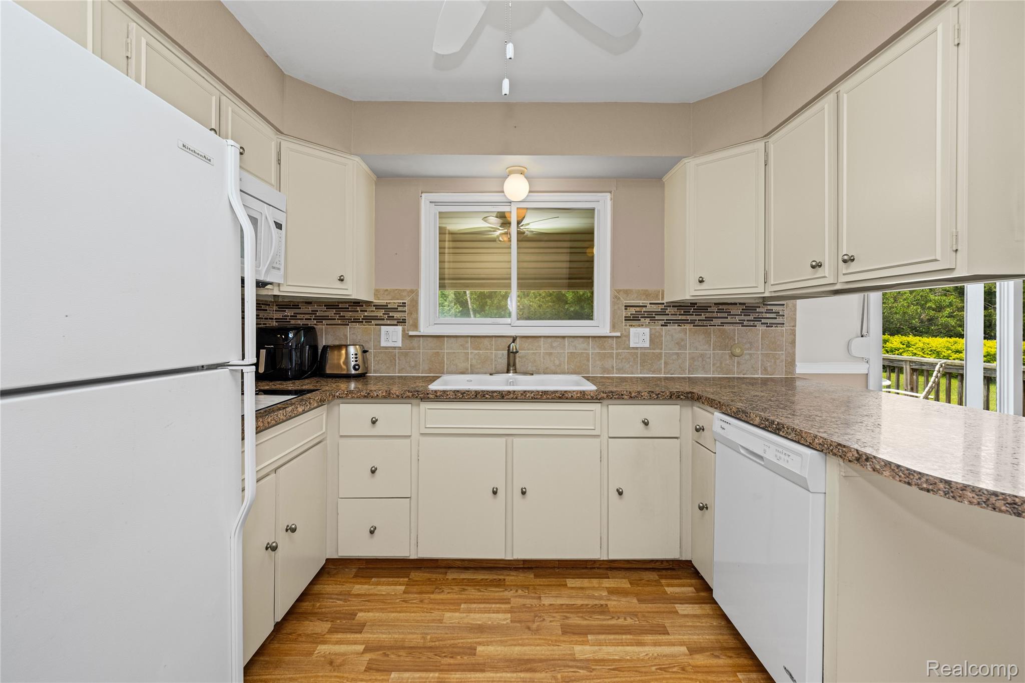 14743 Newburgh Road Livonia, MI 48154 - Photo 15 of 48 U-shaped kitchen featuring cream cabinetry, a white basin sink, mosaic tile backsplash, wood-finish flooring, and solid surface countertops