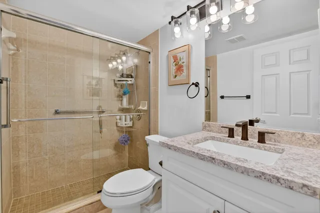 a bathroom with a granite countertop sink a toilet a mirror a vanity and shower