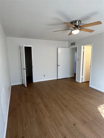 a view of an empty room with wooden floor and a ceiling fan