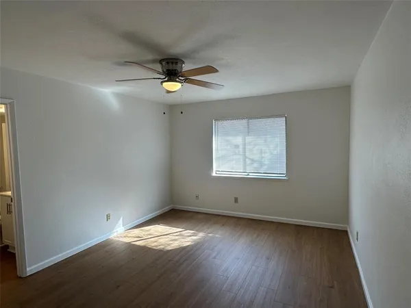 an empty room with wooden floor chandelier fan and windows
