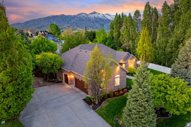 6208 West Bull River Road Highland, UT 84003 - Photo 75 of 90 Brick exterior residence featuring a concrete driveway, multi-car garage with wood-finish doors, manicured landscaping, and mature trees