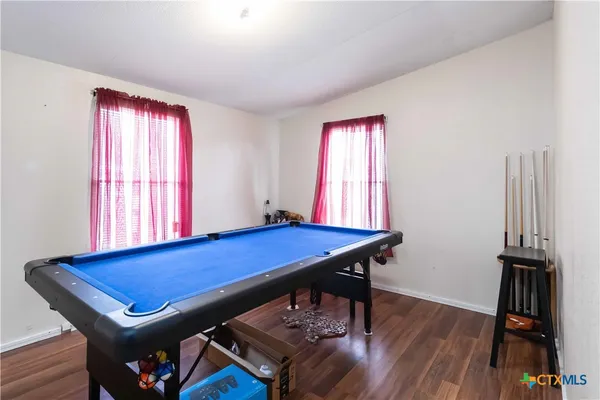 a room with pool table two windows and a wooden floor