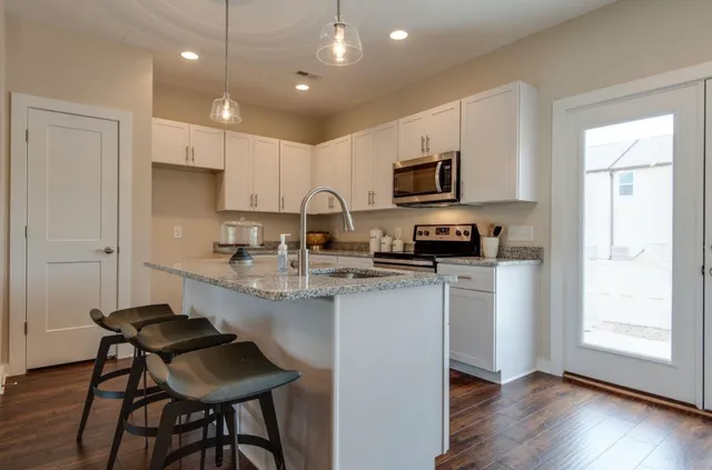 a kitchen with stainless steel appliances granite countertop a stove a sink a microwave a refrigerator and white cabinets with wooden floor