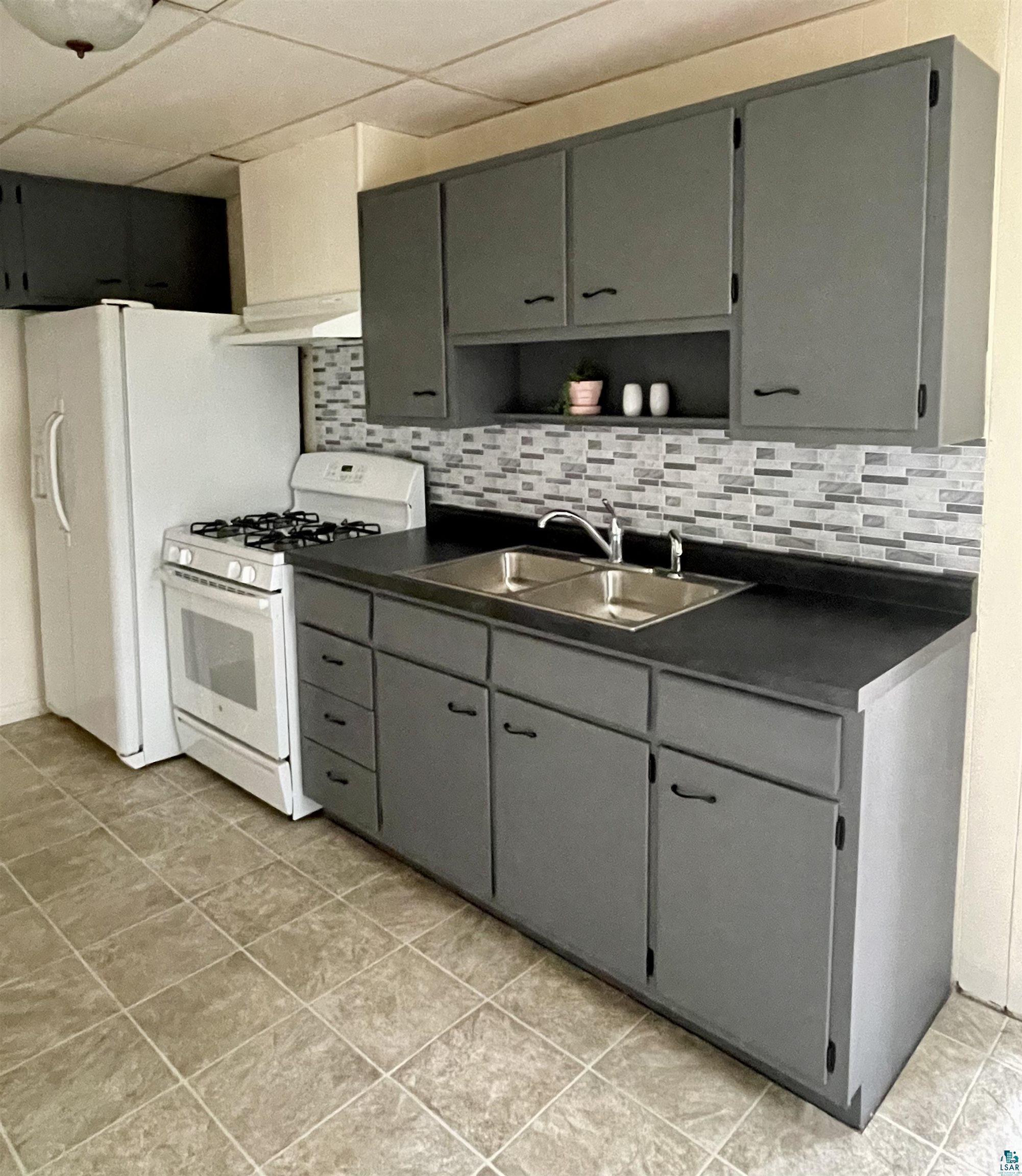 Kitchen featuring white gas range, tasteful backsplash, a paneled ceiling, light tile floors, and sink