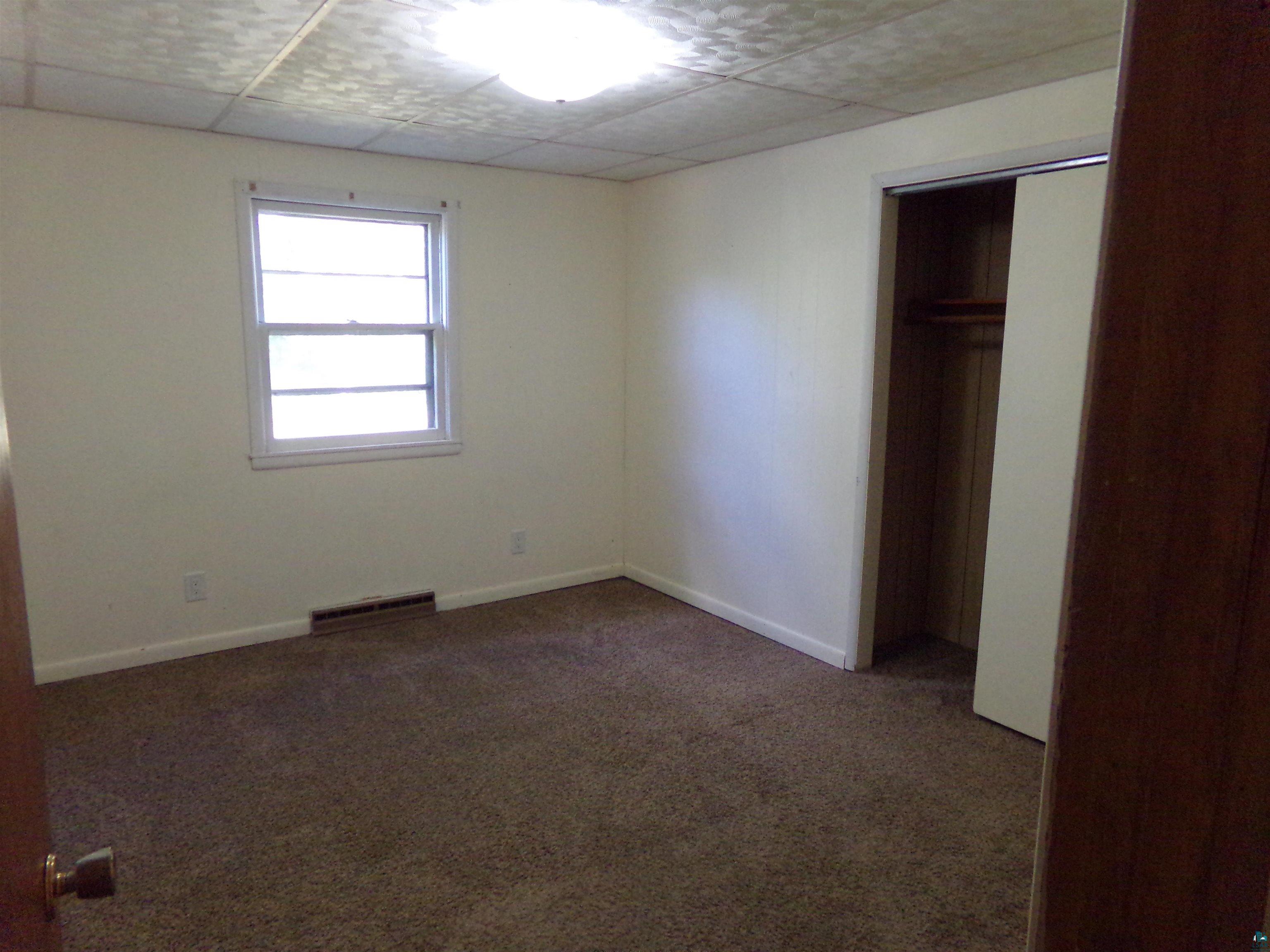 Unfurnished bedroom with a closet, dark carpet, and a drop ceiling
