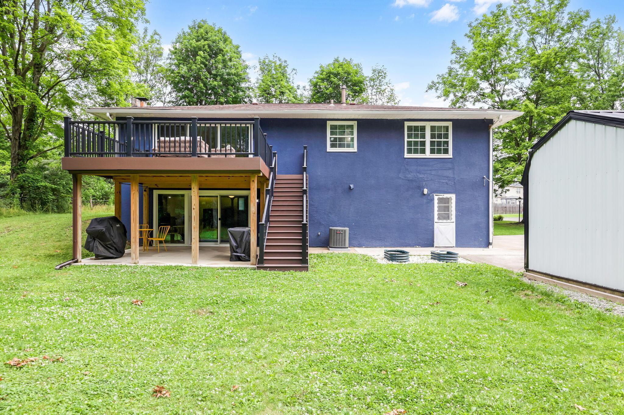 14823 Cleveland Road Southwest Pataskala, OH 43062 - Photo 39 of 57 Rear exterior featuring a blue stucco finish, a raised deck with dark railing, and a ground-level patio