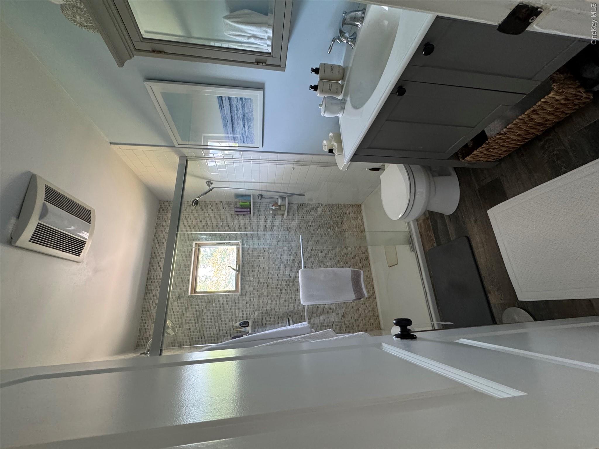 338 Carnation Road West Islip, NY 11795 - Photo 6 of 18 Full bathroom featuring a glass-enclosed shower with mosaic tile surround, a single vanity with a white countertop and undermount sink, wood-finish flooring, and a recessed ceiling fan with integrated lighting