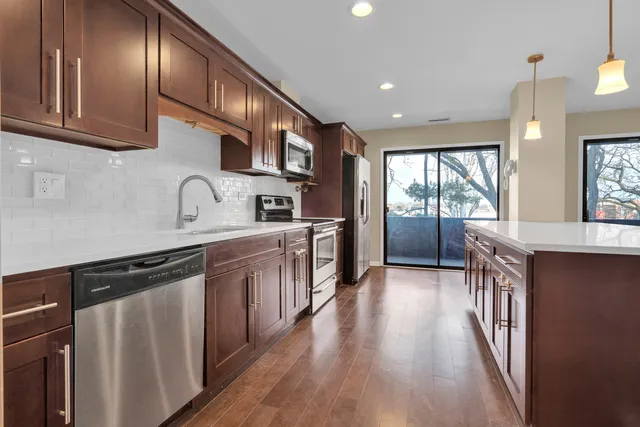 a kitchen with stainless steel appliances granite countertop a refrigerator a sink dishwasher a stove and white countertops with wooden floor