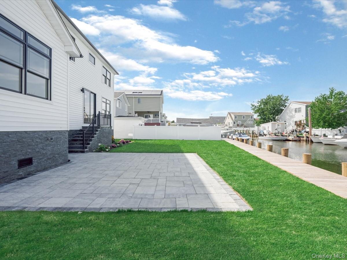 2849 Alder Road Bellmore, NY 11710 - Photo 22 of 34 Spacious backyard featuring a stone paver patio, lush green lawn, and a private wooden dock leading to the canal