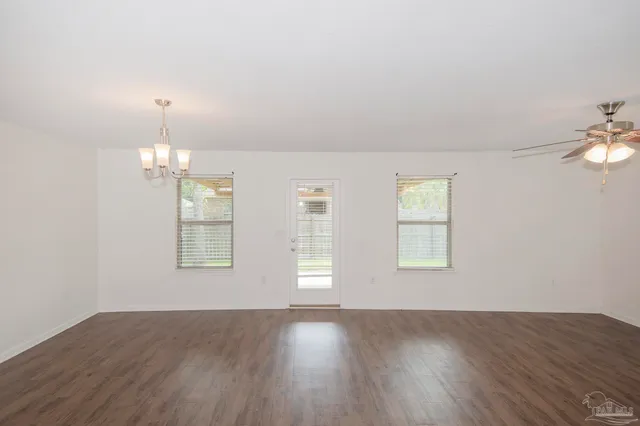 an empty room with wooden floor chandelier and windows