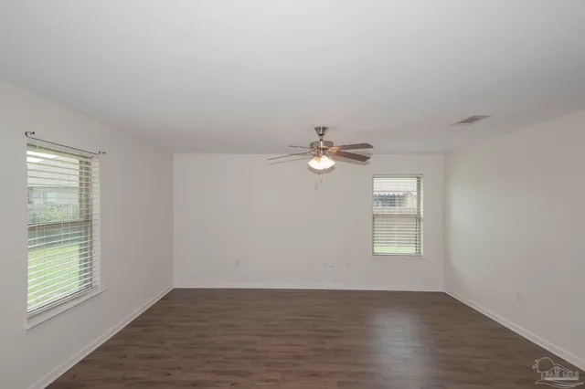 an empty room with wooden floor chandelier fan and windows