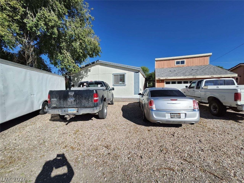 942 Holt Caliente, NV 89008 - Photo 5 of 22 A gravel parking area offers ample space for vehicles, complemented by a modest structure and mature trees.