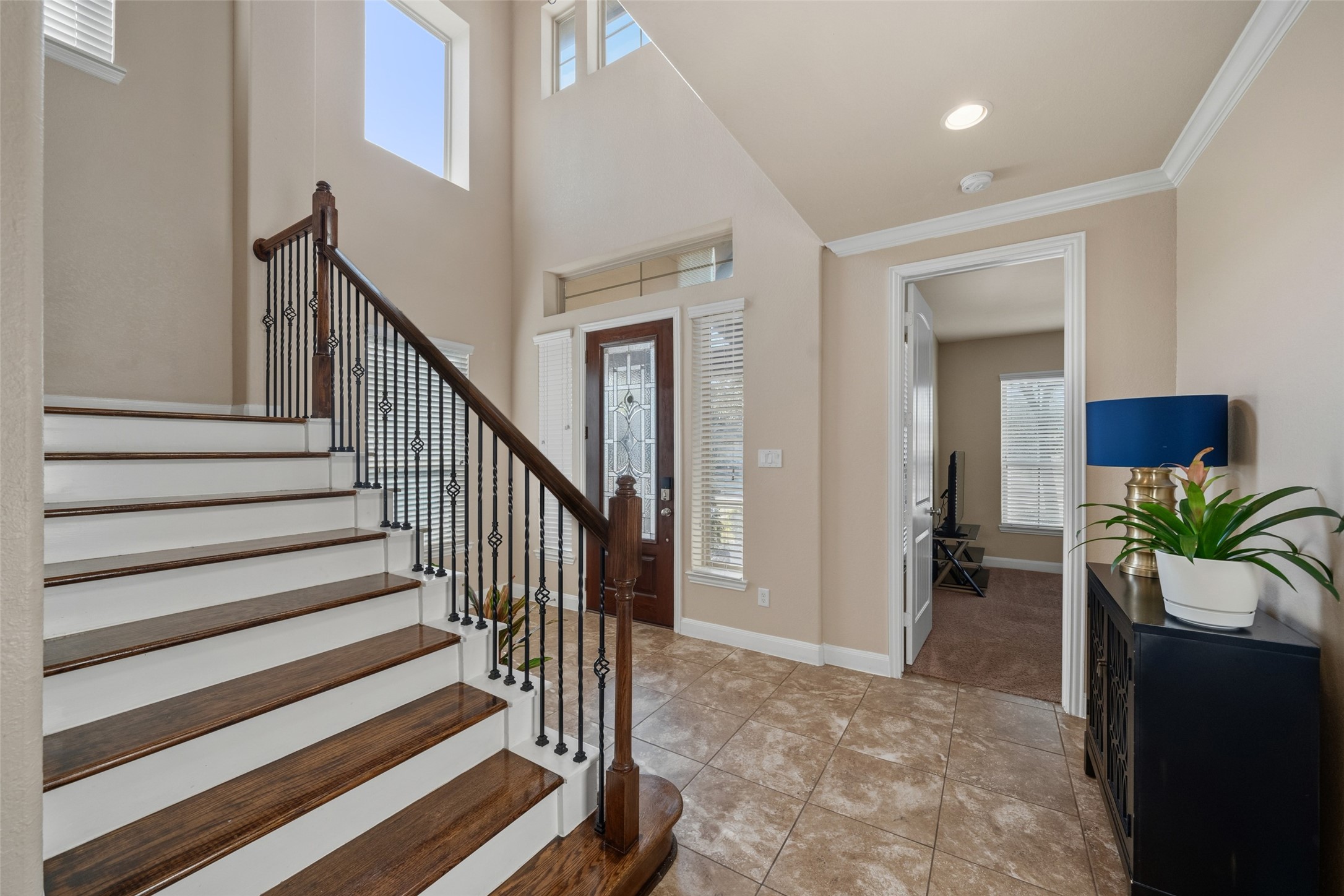 4747 Abercorn Street Rosharon, TX 77583 - Photo 5 of 46 Bright and welcoming entryway with high ceilings and large windows. Features a stylish staircase with wooden steps and wrought iron railing, tiled flooring, and access to a cozy room with carpet. Ideal for a modern and inviting home.