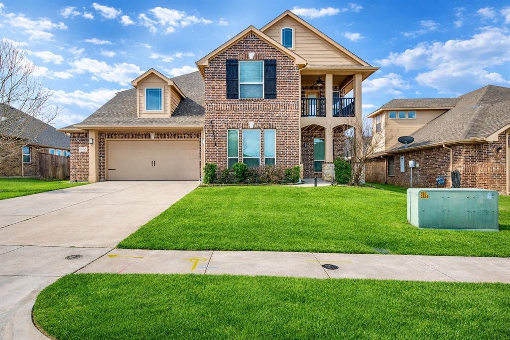 View of front facade with a balcony, a front lawn, brick siding, and driveway