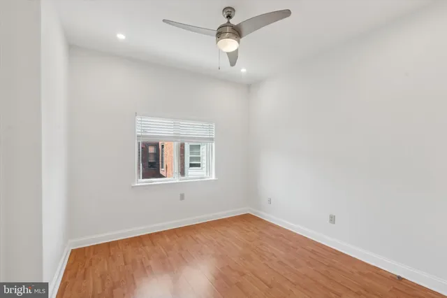 an empty room with wooden floor ceiling fan and window