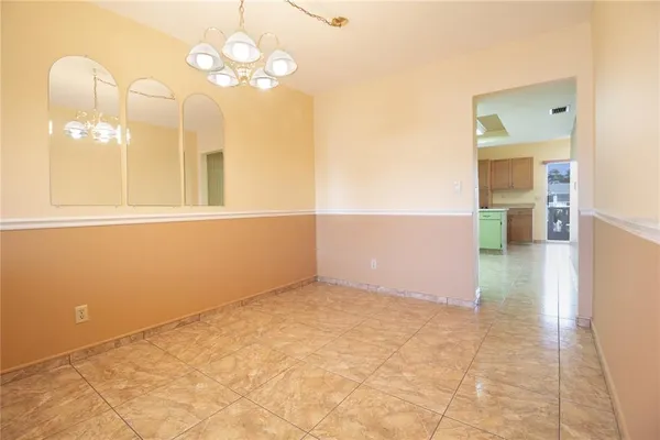 en empty room with kitchen view and a chandelier