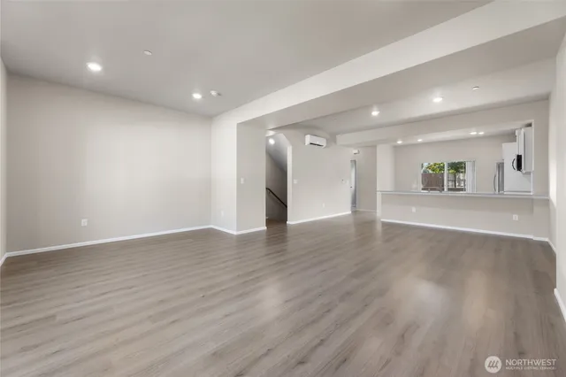 a view of an empty room with wooden floor and a kitchen
