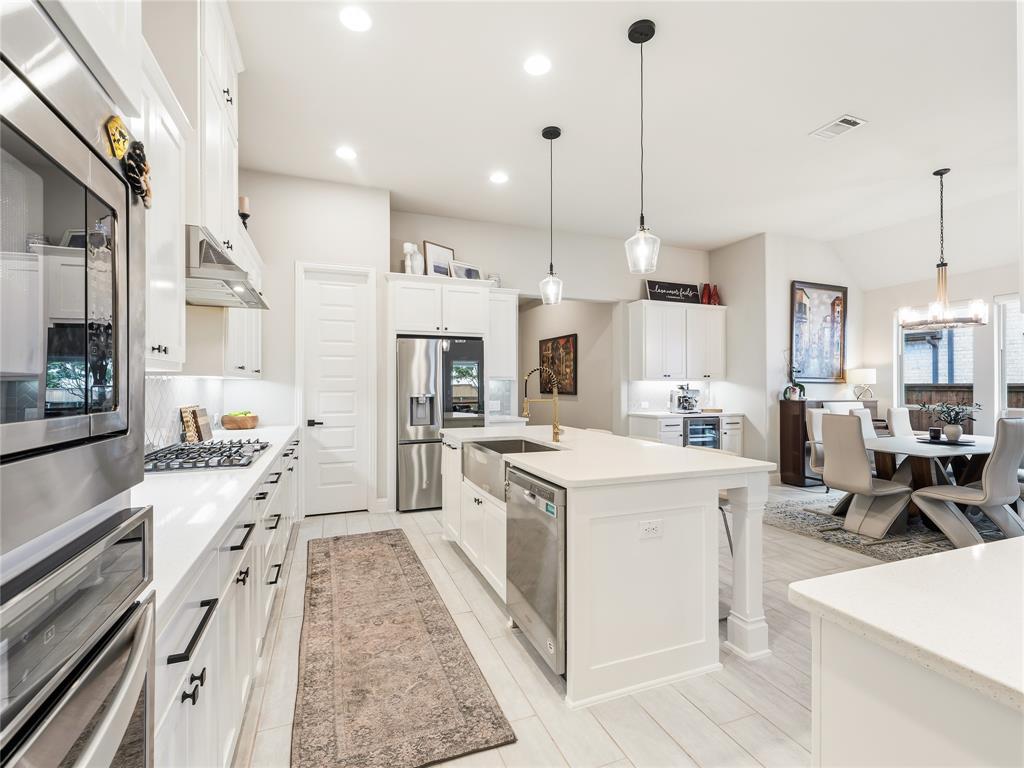 15340 Crape Myrtle Road Frisco, TX 75035 - Photo 11 of 40 Gourmet kitchen featuring a central island, stainless steel appliances, white cabinetry, quartz countertops, and wood-finish flooring