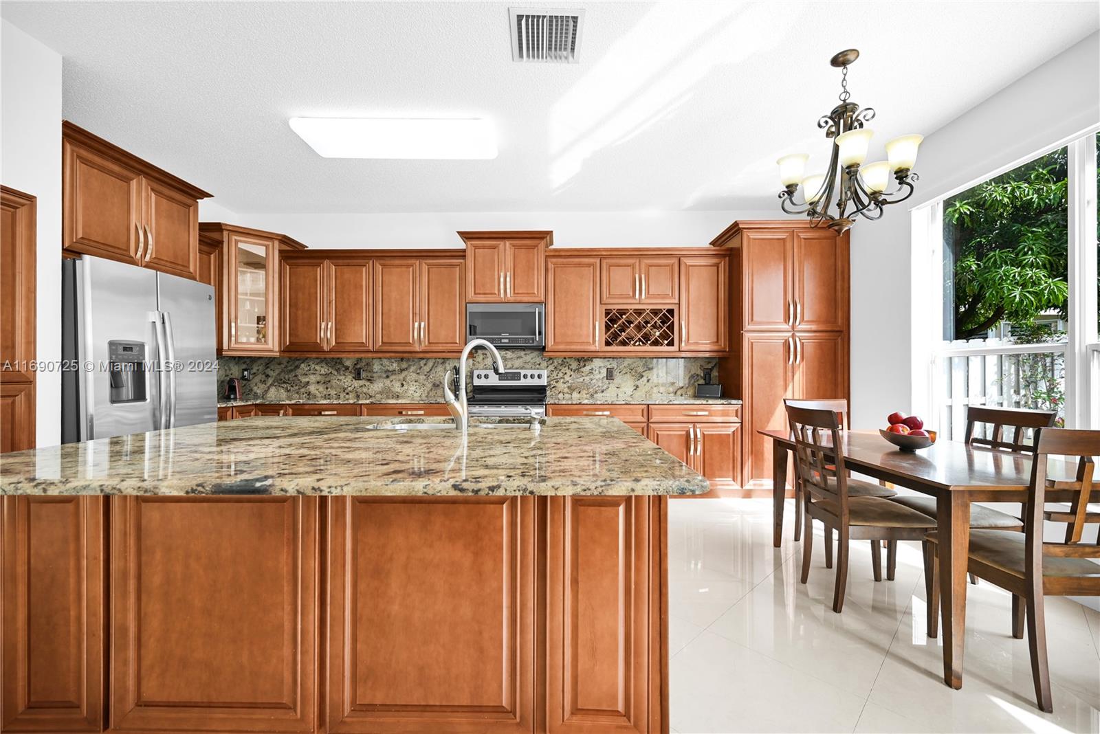 2497 Southwest 163rd Avenue Miramar, FL 33027 - Photo 9 of 50 a kitchen with stainless steel appliances granite countertop a stove top oven a sink a dining table and chairs with wooden floor