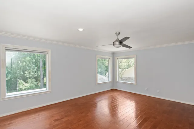 an empty room with wooden floor chandelier fan and windows