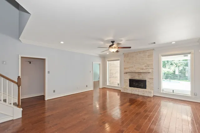 an empty room with wooden floor fireplace cabinet and windows