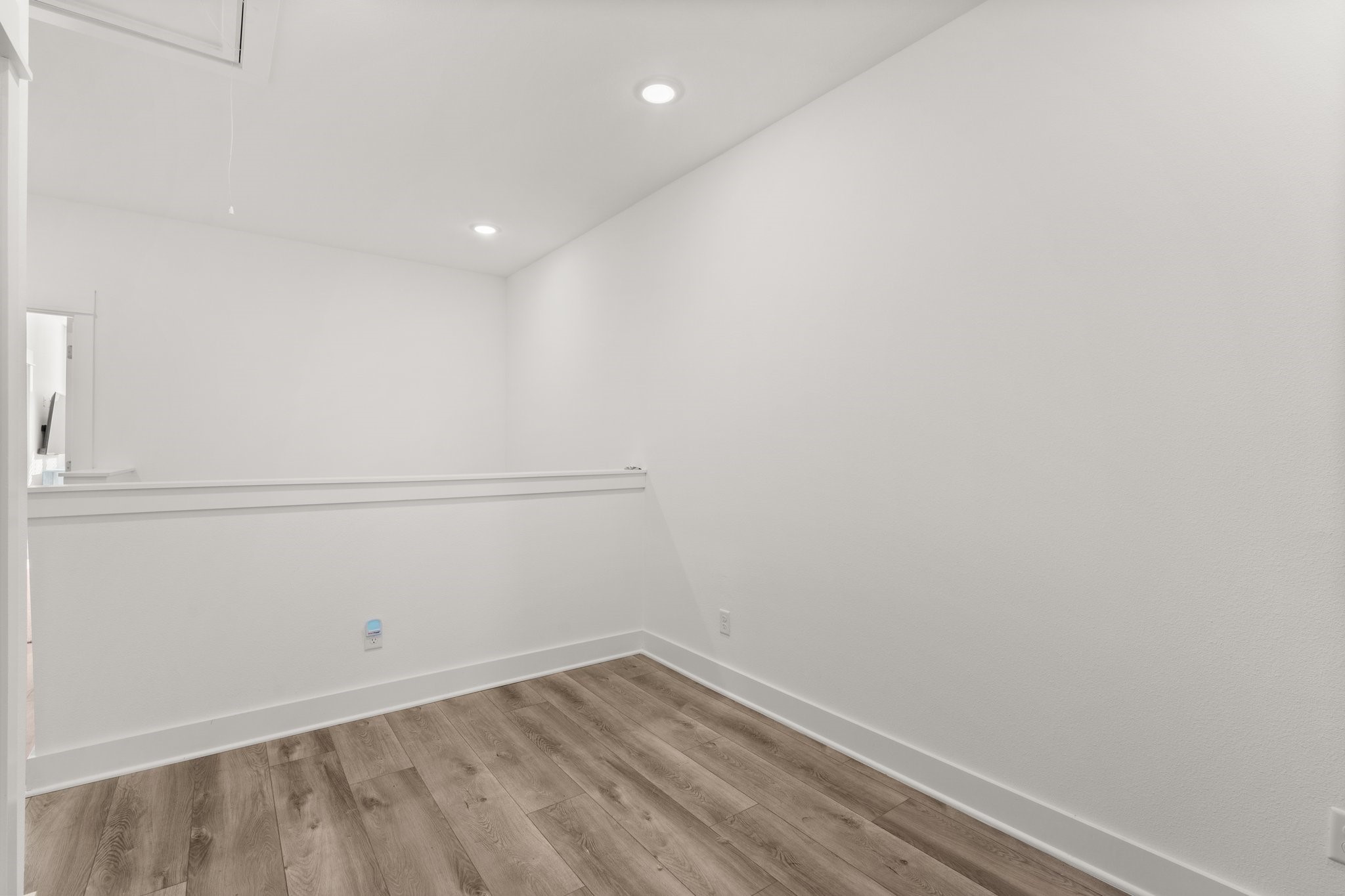 2928 Stevens Street Houston, TX 77026 - Photo 17 of 30 This photo shows a small, bright room with white walls, recessed lighting, and wood-style flooring. A half-wall adds dimension, making it suitable for a cozy office or reading nook.