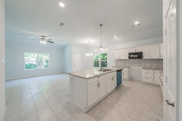 a large kitchen with granite countertop a sink and dishwasher a stove top oven with white cabinets