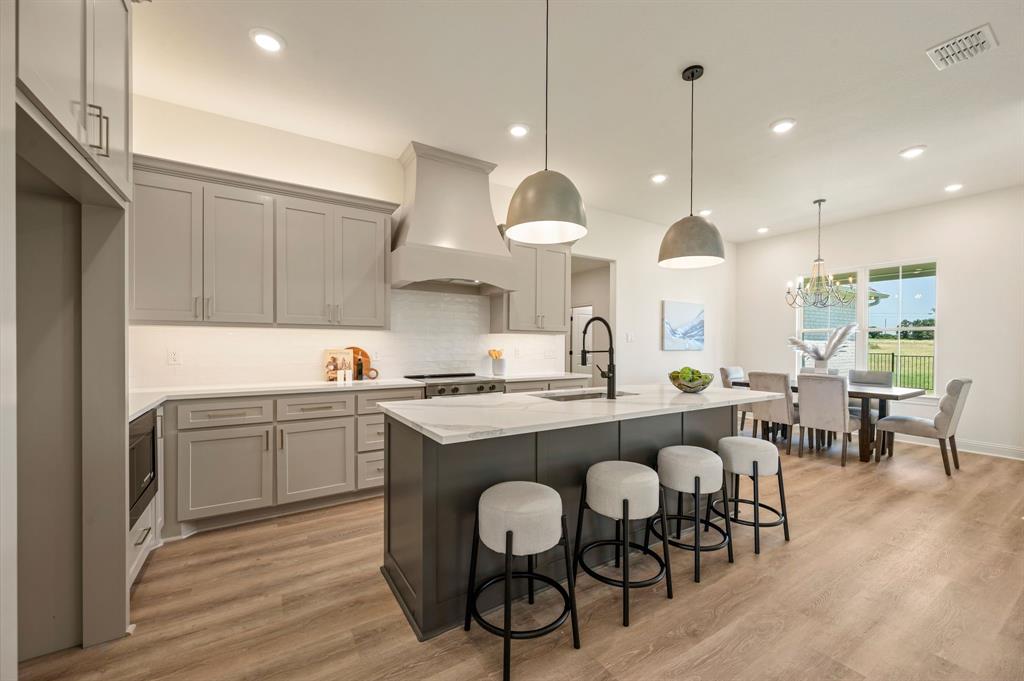 2705 Gospel Road Tolar, TX 76476 - Photo 12 of 36 Modern kitchen featuring light gray cabinetry, an island with a white stone countertop, integrated sink, and black faucet, and luxury vinyl flooring