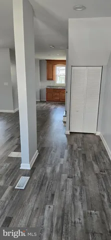 a view of a hallway to an empty room with wooden floor and a window