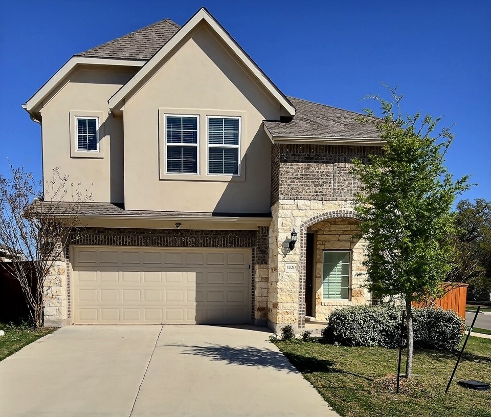 View of front facade featuring stone siding, roof with shingles, driveway, a garage, and stucco siding