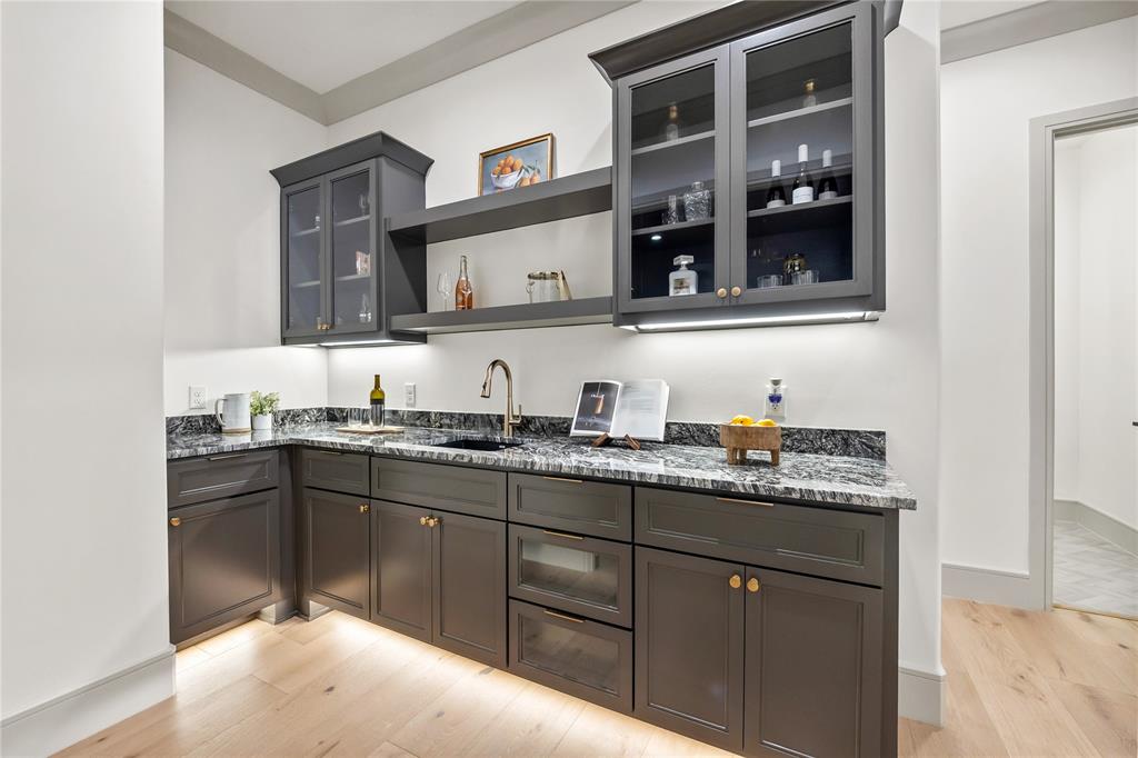 724 Cooper Trail Weatherford, TX 76087 - Photo 23 of 37 Built-in wet bar featuring dark cabinetry, granite countertops, an undermount sink with a gooseneck faucet, display shelving, and light wood-finish flooring