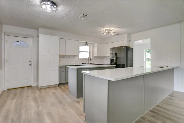 a kitchen with granite countertop a refrigerator a sink dishwasher and white cabinets with wooden floor