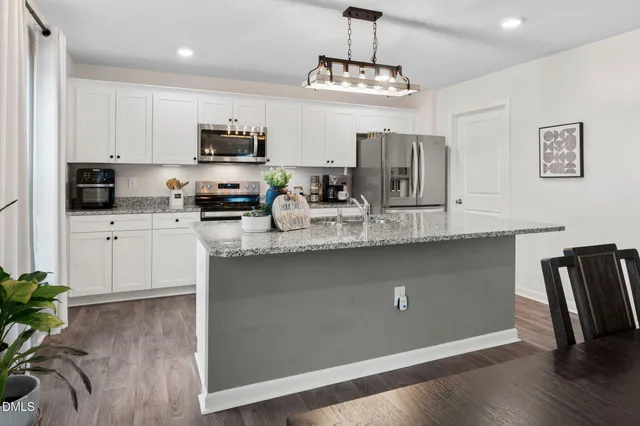 a kitchen with kitchen island granite countertop stainless steel appliances a sink a stove a refrigerator cabinets and wooden floor