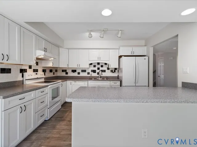 a kitchen with stainless steel appliances kitchen island granite countertop a refrigerator a sink dishwasher and white cabinets with wooden floor