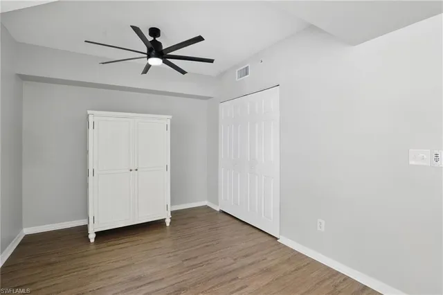 a view of an empty room with wooden floor and a ceiling fan