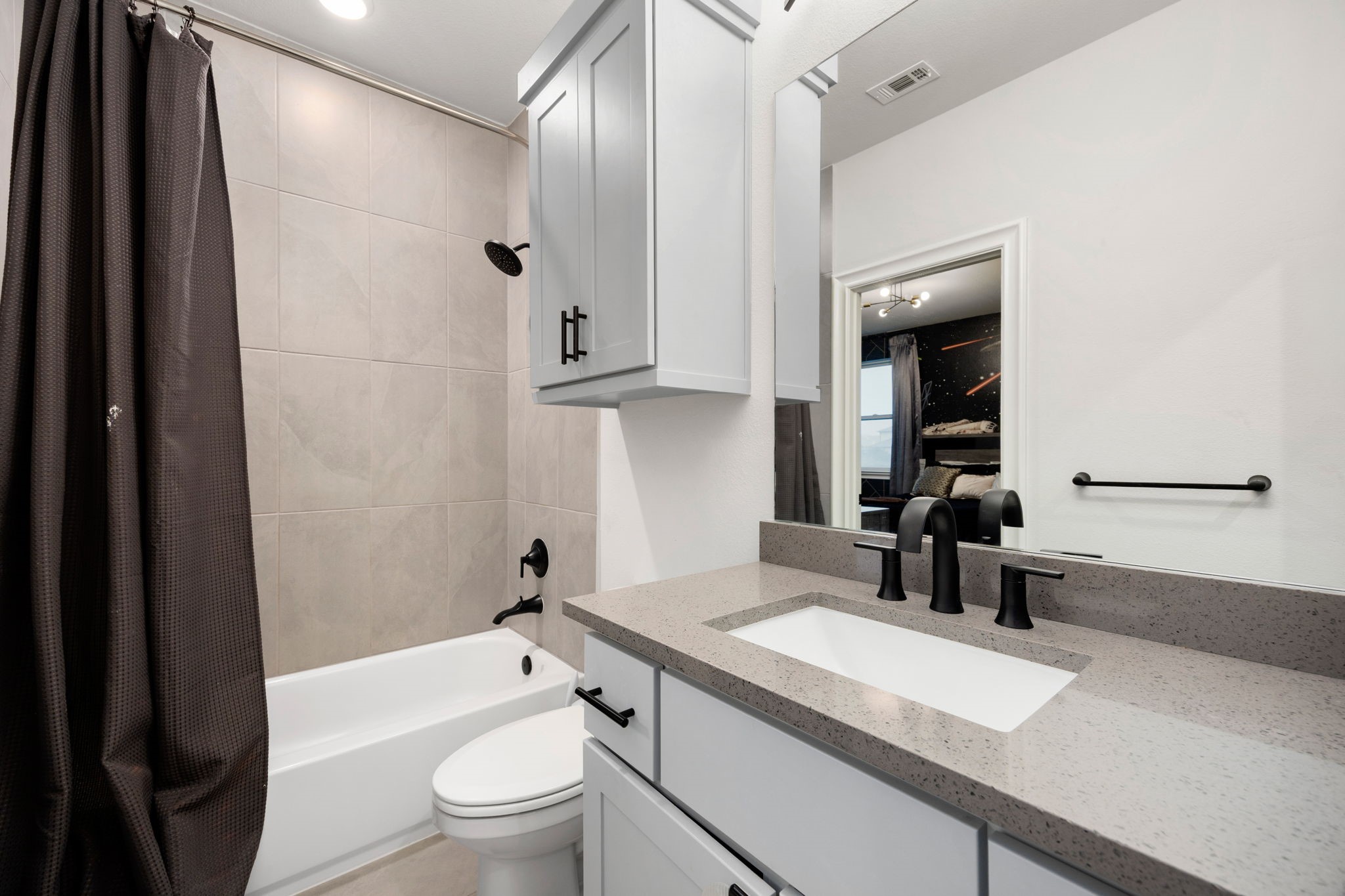 29419 Cir S Rnch Trail Fulshear, TX 77406 - Photo 26 of 45 The secondary en-suite bathroom includes a white storage vanity with a solid quartz counter, black plumbing fixtures, a matching storage cabinet, and a clean tub/shower combo layout.