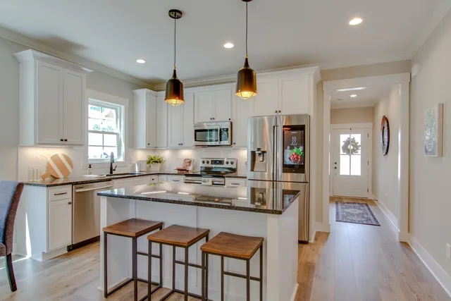 a kitchen with stainless steel appliances granite countertop a stove a sink a refrigerator and chairs with wooden floor