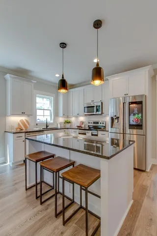 a kitchen with kitchen island stainless steel appliances a dining table chairs sink and cabinets