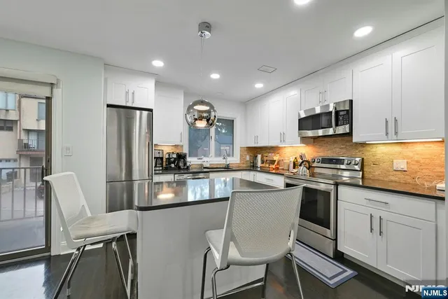 a kitchen with stainless steel appliances granite countertop a stove a sink a refrigerator white cabinets and chairs