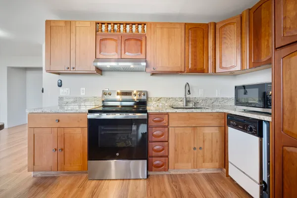 a kitchen with stainless steel appliances granite countertop a stove a sink dishwasher and a refrigerator with wooden cabinets