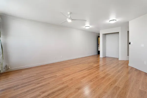 a view of an empty room with wooden floor and a ceiling fan