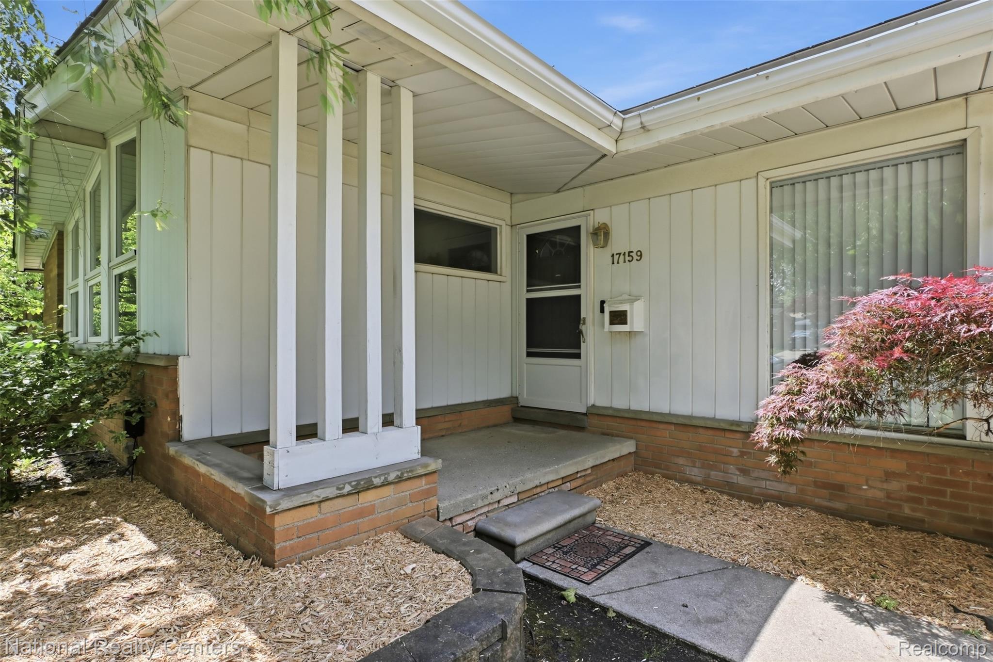 17159 Rougeway Street Livonia, MI 48152 - Photo 4 of 36 Mid-century modern exterior featuring vertical siding, a brick foundation, a covered entry, and a large front window with vertical blinds