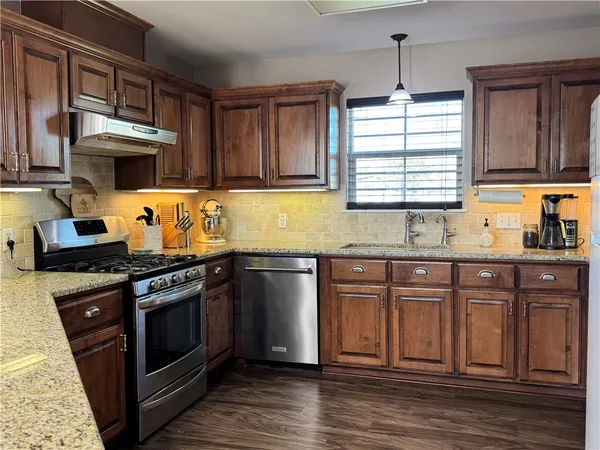 a kitchen with stainless steel appliances granite countertop a stove a sink dishwasher and a microwave oven with wooden cabinets