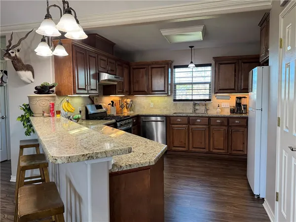 a kitchen with stainless steel appliances granite countertop wooden cabinets a stove a sink and a refrigerator