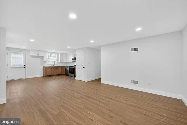 a view of an empty room with wooden floor and kitchen