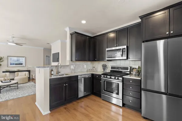 a kitchen with stainless steel appliances granite countertop a refrigerator a sink dishwasher a stove and a dining table with wooden floor
