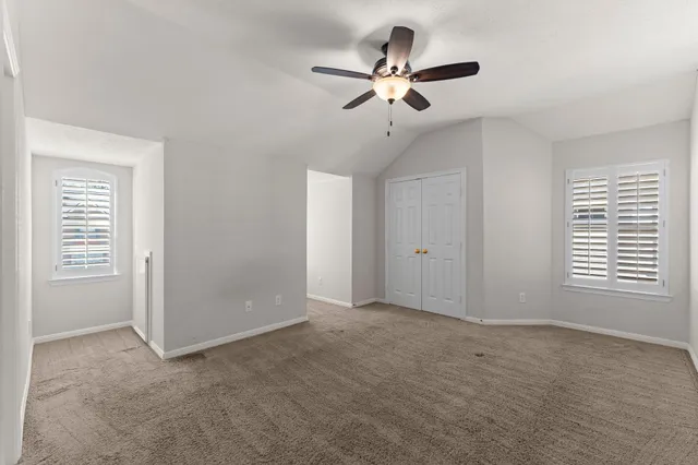 an empty room with chandelier fan and windows